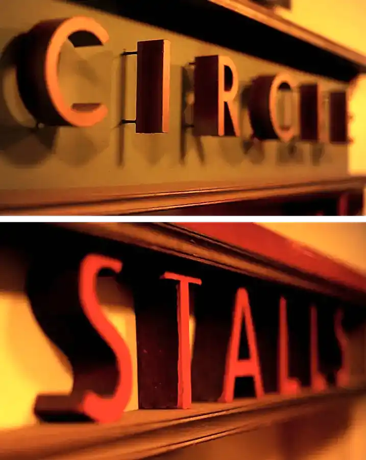 Close-ups of two art-deco style cinema door signs. One reads 'circle', the other 'stalls'.