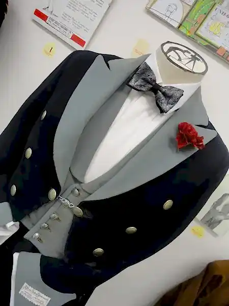 A headless mannequin wearing a bow tie and a uniform tail coat with brass coloured buttons and a red carnation 'buttonhole'. The photo is composed using a 'dutch angle'.