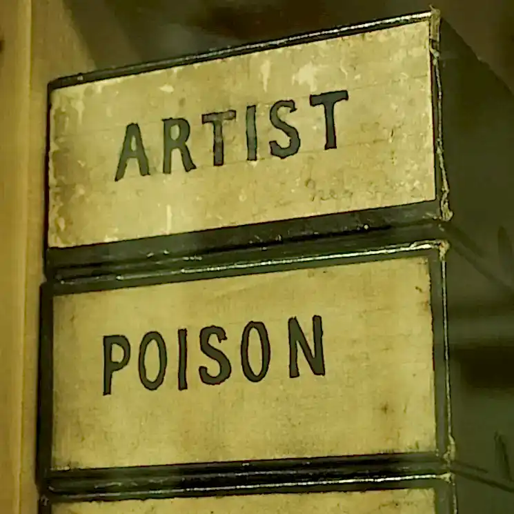 Two cardboard boxes, designed to hold short reels of film. One is labelled 'Artist', the other 'Poison'.