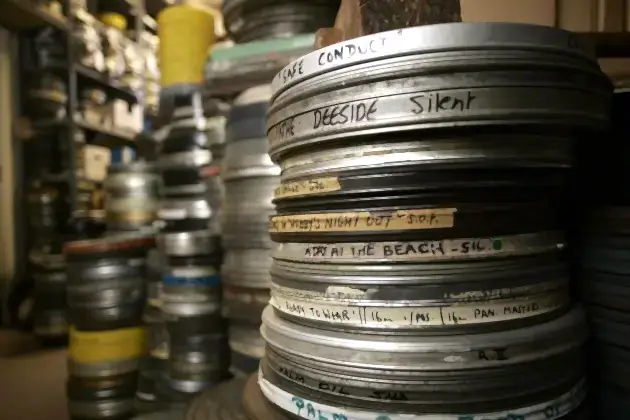 A stack of 35mm film canisters with many more of the same out of focus in the background. The canisters are labelled by hand around their edges.