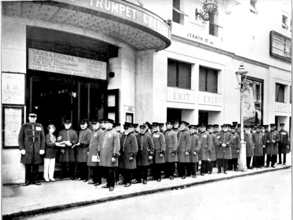A large group of Chelsea Pensioners queuing outside a cinema to see a 1915 film entitled 'The Trumpet Call'.