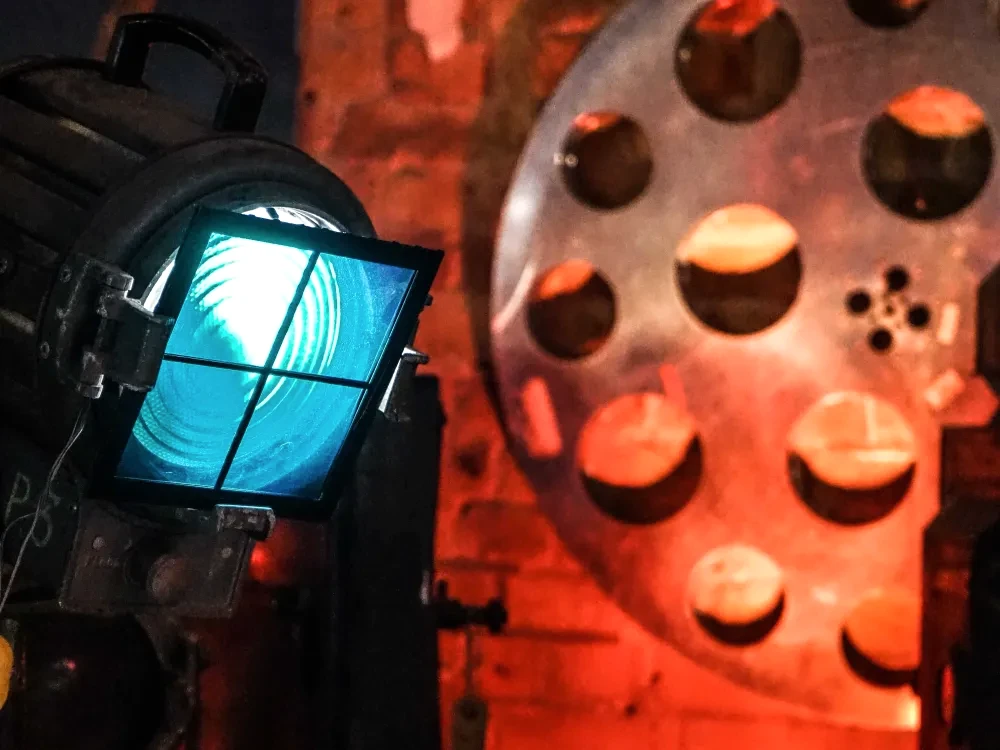 A spotlight shining in a darkened room, with a brick wall and large cinema film reel in the background.