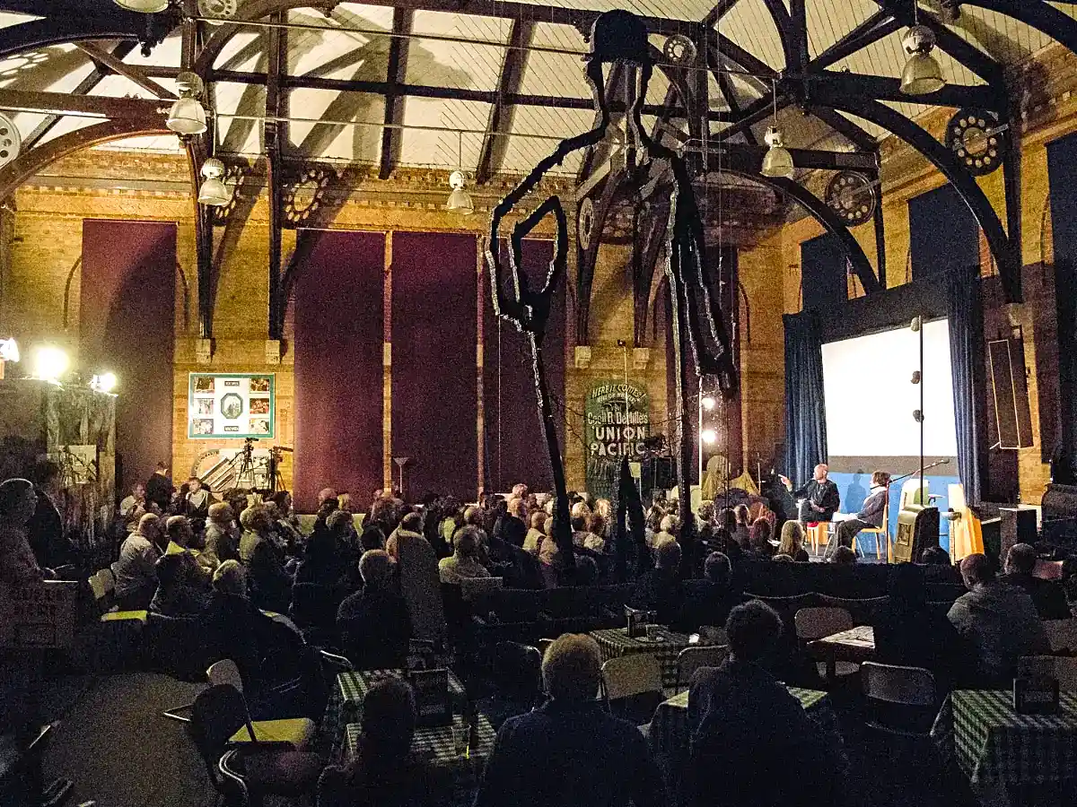 The main hall at the museum, a seated audience is watching an interview on stage.